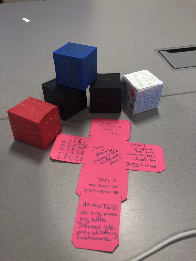 a stack of poetry cubes in multiple colors. One cube is not yet folded, so it lies flat in a cross-shape. 