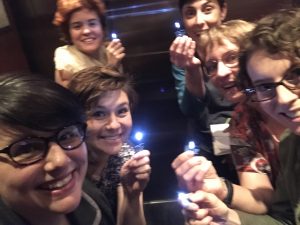 Six women in a semi-darkened elevator, holding their soldered flashlight projects