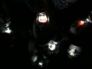 Three or four women holding flashlights up to their faces in a darkened room