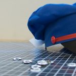 Pretend mail carrier hat sitting on a cutting mat, surrounded by grommets